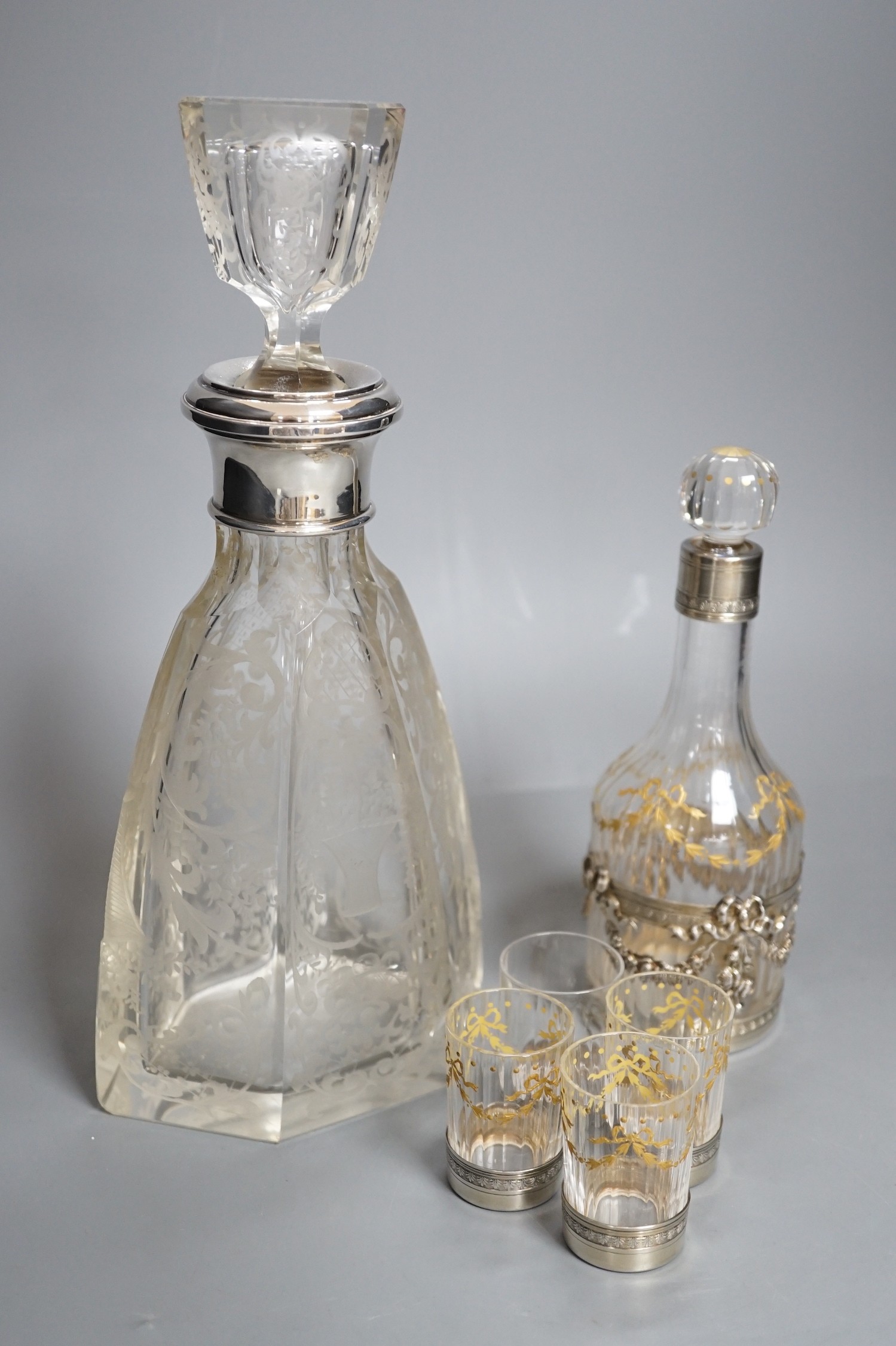 An early 20th century French white metal mounted gilded glass decanter and stopper and four matching tots, decanter height 19.7cm, and a French white metal collared etched glass decanter and stopper.